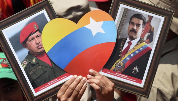 Apoiador(a) do presidente venezuelano, Nicolás Maduro, exibe imagens do atual chefe de Estado e de seu antecessor, Hugo Chávez, durante manifestação em Caracas no Dia do Trabalhador - Sputnik Brasil