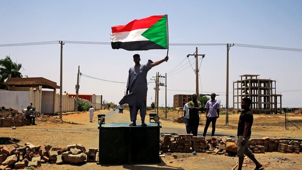 Um manifestante sudanês em Cartum segura uma bandeira nacional ao se deparar com uma barricada ao longo de uma rua, exigindo que o Conselho Militar de Transição do país entregue o poder a civis. - Sputnik Brasil