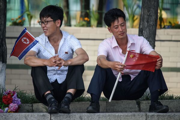 Dois homens segurando bandeiras norte-coreana e chinesa
 - Sputnik Brasil