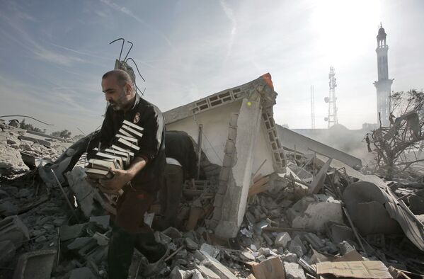 Homem remove pilha de livros do Alcorão de prédio destruído por explosão, Gaza  - Sputnik Brasil