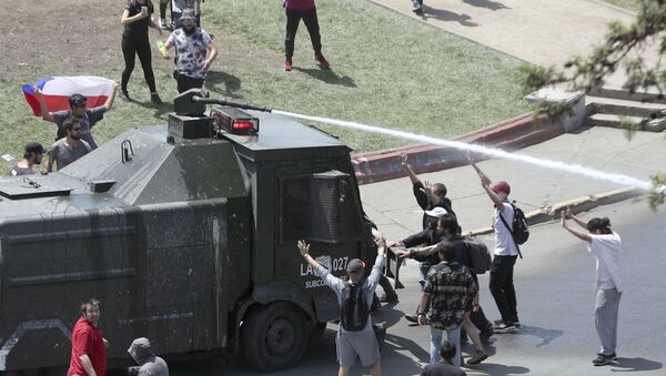 Manifestantes em Santiago, no Chile, confrontam um veículo policial equipado com canhões de água. O registro é do 5º dia de protestos de massa no país, em 22 de outubro de 2019. - Sputnik Brasil