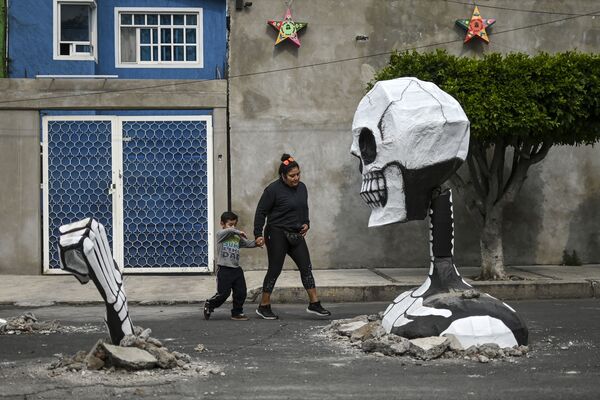 Mulher com uma criança caminhando diante de uma escultura na véspera do Dia dos Mortos no México. Foto tirada em 28 de outubro - Sputnik Brasil