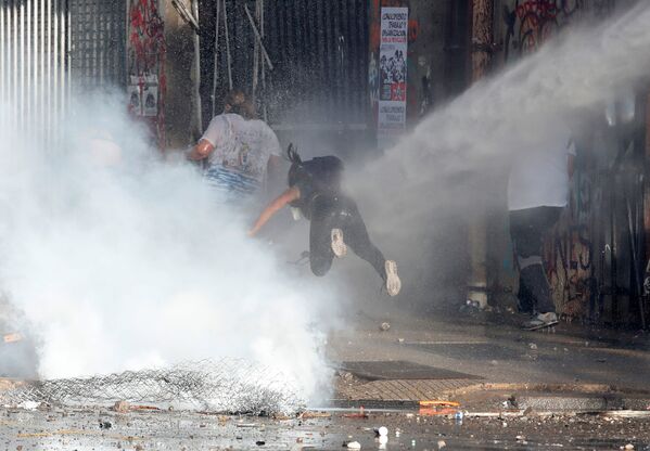 Manifestante é jogada no chão por um canhão de água da Polícia do Chile durante manifestação na capital Santiago - Sputnik Brasil