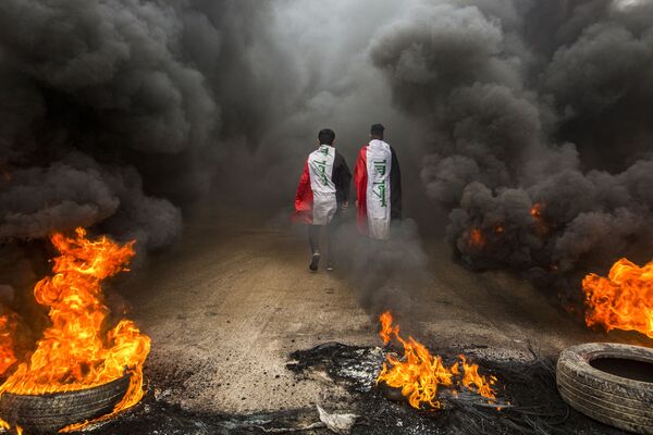 Manifestantes contra o governo iraquiano caminham com bandeiras do país entre chamas na cidade iraquiana de Basra - Sputnik Brasil