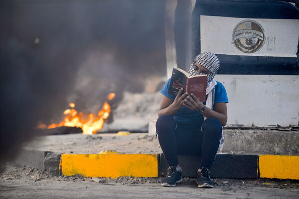Manifestante lê romance sentado próximo de pneus queimados durante manifestação no Iraque
 - Sputnik Brasil