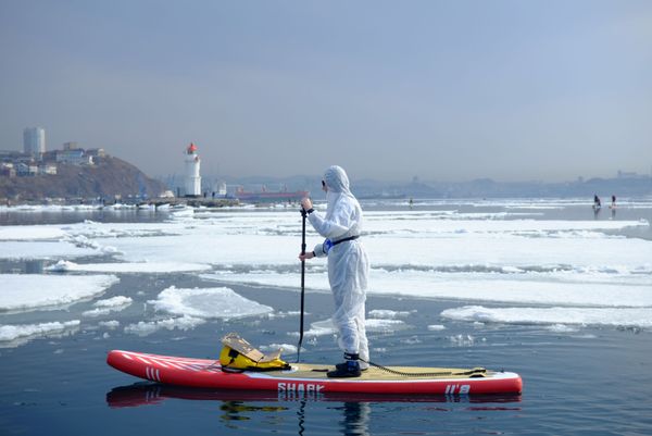 Homem com traje de proteção contra coronavírus sobre prancha em águas de Vladivostok, Rússia, 21 de março de 2020 Homem com traje de proteção contra coronavírus sobre prancha em águas de Vladivostok, Rússia, 21 de março de 2020 - Sputnik Brasil