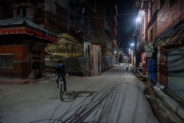 Homem usando máscara de proteção anda de bicicleta em rua na periferia de Katmandu, capital do Nepal - Sputnik Brasil
