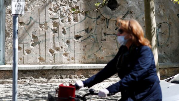 Mulher com máscara para se proteger do coronavírus passa com bicicleta por rua de Berlim, na Alemanha - Sputnik Brasil