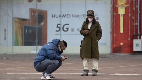 Moradores usando máscaras verificam seus celulares perto de um anúncio de Huawei - Sputnik Brasil