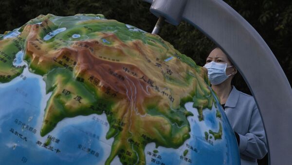 Mulher usando máscara contra coronavírus olha para globo mostrando a China, em Wuhan, na província de Hubei, 15 de abril de 2020 - Sputnik Brasil