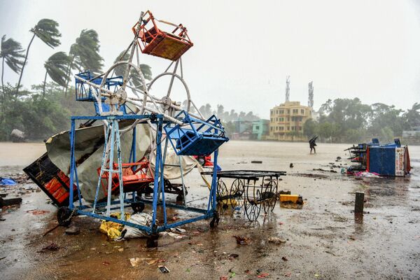 Homem segurando guarda-chuva passa por pequena roda-gigante danificada na praia em Alibag, na Índia, em 3 de junho de 2020 - Sputnik Brasil