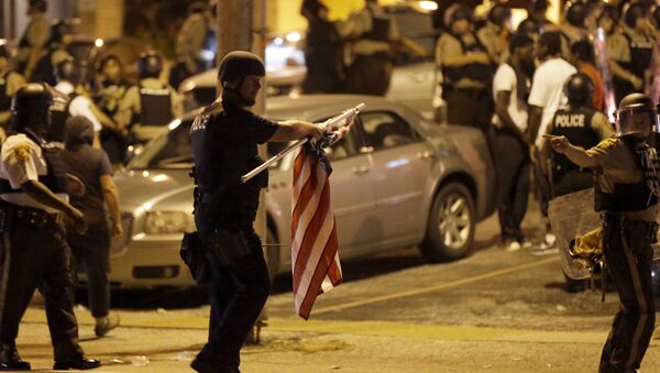 Policial com uma bandeira estadunidense que ele tomou de um manifestante durante os protestos em Ferguson, Missouri - Sputnik Brasil