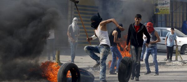 A Palestinian protester moves a burning tyre during clashes with the Israeli army at Qalandia checkpoint near occupied West Bank city of Ramallah October 6, 2015 - Sputnik Brasil