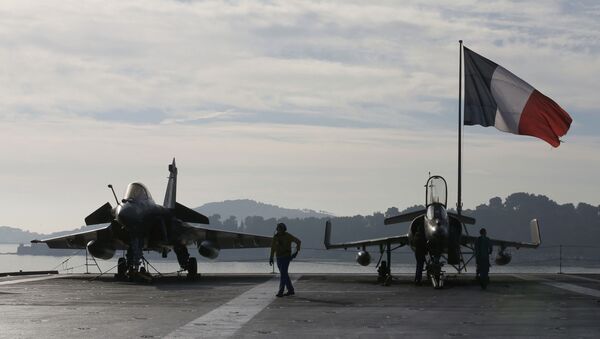 Flight deck crew work around a Rafale (L) and a Super Etendard fighter jets as a French flag flies aboard the French nuclear-powered aircraft carrier Charles de Gaulle before its departure from the naval base of Toulon, France, November 18, 2015 - Sputnik Brasil