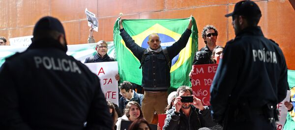 Polícia olha para um manifestante que se cobre com uma bandeira do Brasil e outros que mostram cartazes pró-democracia durante a conferência na Universidade de Lisboa em 31 de março - Sputnik Brasil