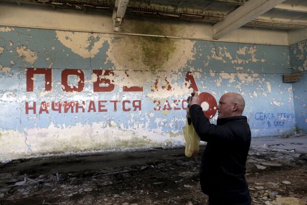 Um homem tira fotos em pavilhão esportivo perto da cidade de Skrunda, Letônia, 9 de abril, 2016. As palavras em russo pintadas na parede significam “Vitória começa aqui” - Sputnik Brasil