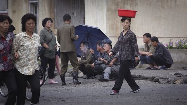 Uma mulher norte-coreana equilibra um balde na cabeça, enquanto homens fumam na rua no final de um dia de trabalho, na quarta-feira, 22 de junho de 2016, em Wonsan, Coreia do Norte. - Sputnik Brasil