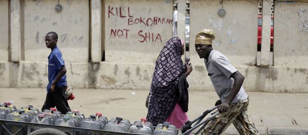 Um jovem passa por uma rua da cidade nigeriana de Kano transportando água, em 8 de abril de 2016; a inscrição na parede diz: Mate Boko Haram e não xiitas - Sputnik Brasil