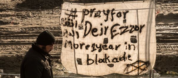 Uma pessoa passa em Calais, França, perto de um cartaz dizendo, em inglês: Ore por Deir ez-Zor, mais de 1 ano sob sítio - Sputnik Brasil
