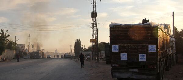 Smoke rises in the distance as Syrians gather near damaged trucks carrying aid on the side of the road in the town of Orum al-Kubra on the western outskirts of the northern Syrian city of Aleppo on September 20, 2016, the morning after a convoy delivering aid was hit by a deadly air strike - Sputnik Brasil