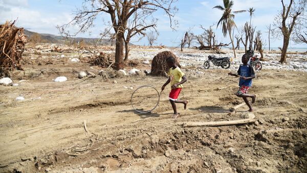Meninos empurram um pneu entre as ruínas da cidade de Les Cayes (Haiti), afetada pelo furacão Matthew - Sputnik Brasil