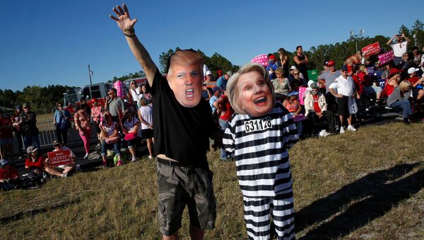 Homem com máscara de Donald Trump ao lado de mulher com máscara de Hillary Clinton, vestida para a prisão, em comício do republicano na Flórida, 23 de outubro de 2016 - Sputnik Brasil