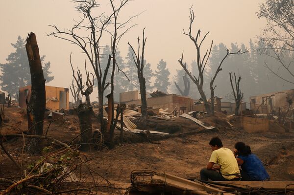 Pessoas sentadas perto de casas destruídas pelos incêndios florestais no povoado de Santa Olga, Chile - Sputnik Brasil