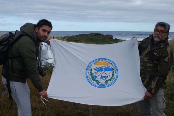 Ex-combatente da Guerra das Malvinas Armando González e seu filho Martín seguram a bandeira de um grupo de heróis do conflito na praia onde se defendeu o regimento - Sputnik Brasil