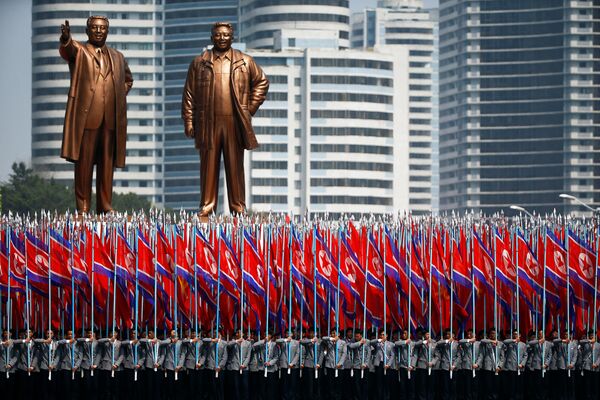 Pessoas carregam bandeiras em frente dos monumentos de Kim Il-sung e Kim Jong-il durante a parada militar comemorativa dem 15 de abril de 2017 - Sputnik Brasil