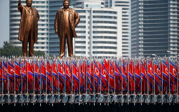 Pessoas carregam bandeiras em frente dos monumentos de Kim Il-sung e Kim Jong-il durante a parada militar comemorativa dem 15 de abril de 2017 - Sputnik Brasil