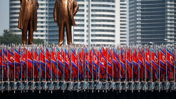 Pessoas carregam bandeiras em frente dos monumentos de Kim Il-sung e Kim Jong-il durante a parada militar comemorativa dem 15 de abril de 2017 - Sputnik Brasil