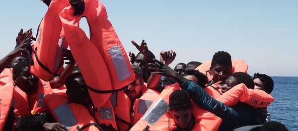 Migrants in an overcrowded plastic raft reach out for life jackets during a search and rescue operation by rescue ship Aquarius, operated by SOS Mediterranean and Doctors without Borders, in central Mediterranean Sea May 18, 2017 - Sputnik Brasil