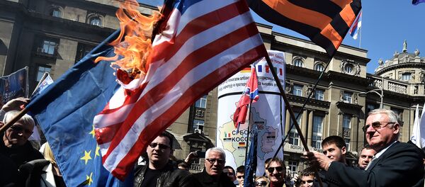 O político nacionalista sérvio Vojislav Seselj cercado por seus apoiadores mantém uma  bandeira da OTAN durante uma manifestação de oposição ao governo (foto de arquivo - 2015). - Sputnik Brasil