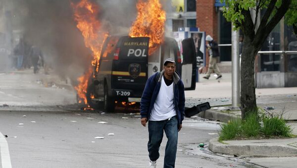A man walks past a burning police vehicle, Monday, April 27, 2015, during unrest following the funeral of Freddie Gray in Baltimore. Gray died from spinal injuries about a week after he was arrested and transported in a Baltimore Police Department van. - Sputnik Brasil