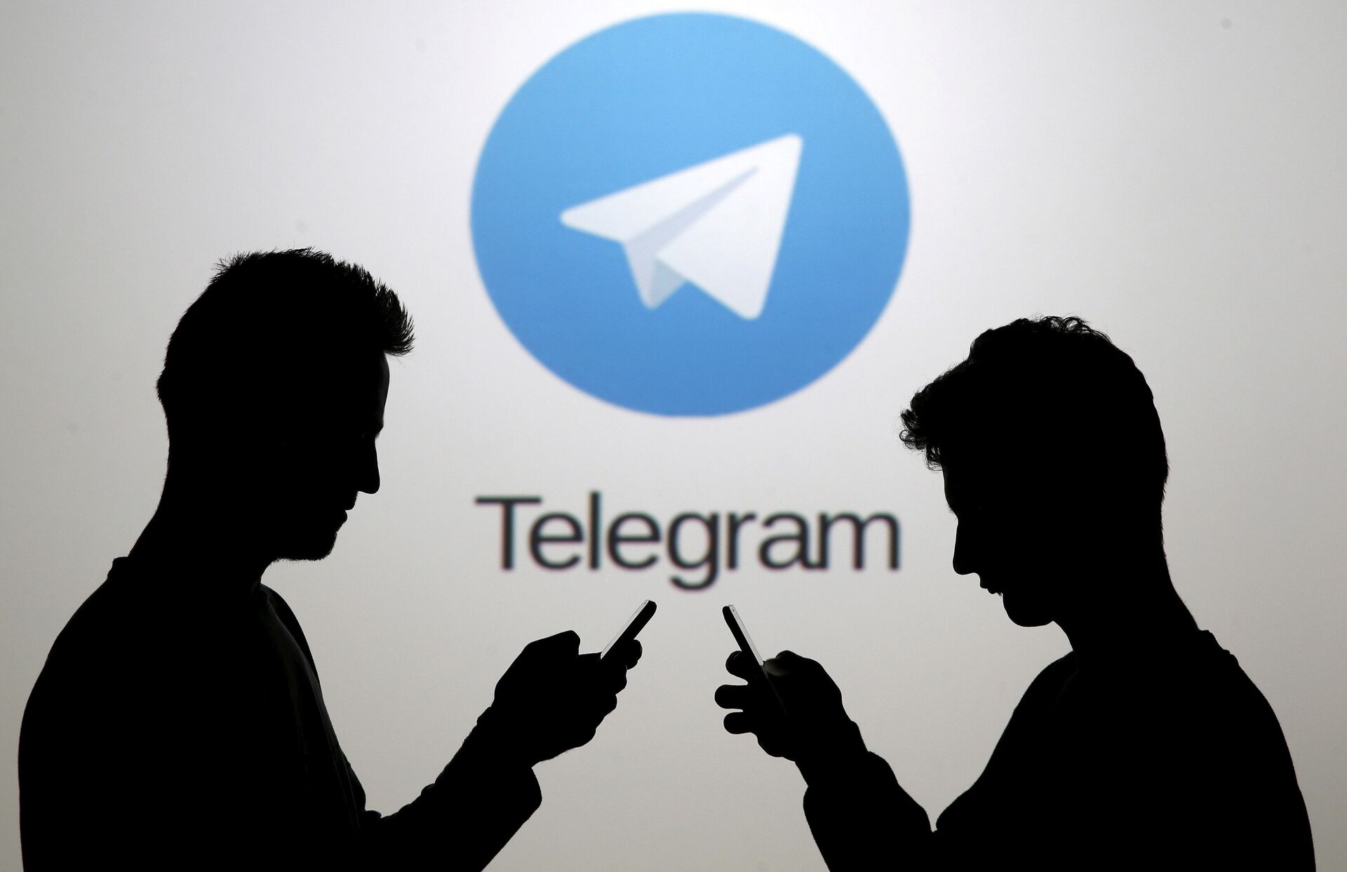Dois homens, usando seus smartphones, estão em frente ao logotipo do Telegram - Sputnik Brasil, 1920, 20.03.2022
