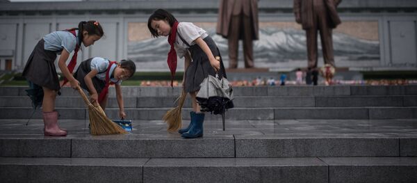 Crianças limpam os degraus perto dos monumentos de Kim Jong-il e Kim Il-sung na Coreia do Norte, no âmbito dos festejos do Dia da Vitória - Sputnik Brasil