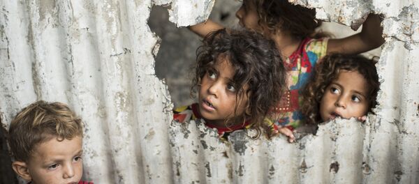 Crianças palestinas olham através de um buraco no cercado em um bairro pobre de Gaza - Sputnik Brasil