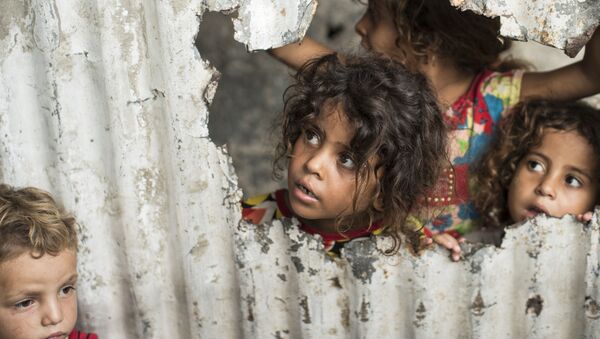 Crianças palestinas olham através de um buraco no cercado em um bairro pobre de Gaza - Sputnik Brasil