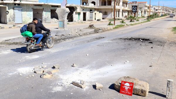 Men ride a motorbike past a hazard sign at a site hit by an airstrike on Tuesday in the town of Khan Sheikhoun in rebel-held Idlib, Syria April 5, 2017 - Sputnik Brasil
