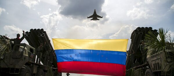 A Russian-made Sukhoi Su-30MKV fighter jet of the Venezuelan Air Force flies over a Venezuelan flag tied to missile launchers, during the Escudo Soberano 2015 (Sovereign Shield 2015) military exercise in San Carlos del Meta in the state of Apure - Sputnik Brasil